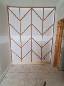 Chevron pattern accent wall with raw wood strips over drywall, unfinished and ready for paint