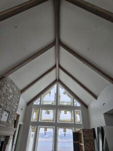 Painted vaulted ceiling peak above a tall multi pane window wall and stone fireplace column