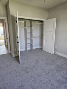 White hinged closet door open, revealing built-in shelving with compartments and closet rods.