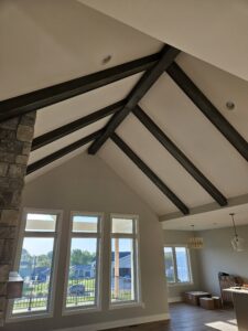 Dark stained wood beams follow the vaulted roofline to a stone chimney and tall windows