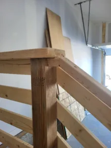 Raw wood horizontal rail with a corner post joint, unfinished stage