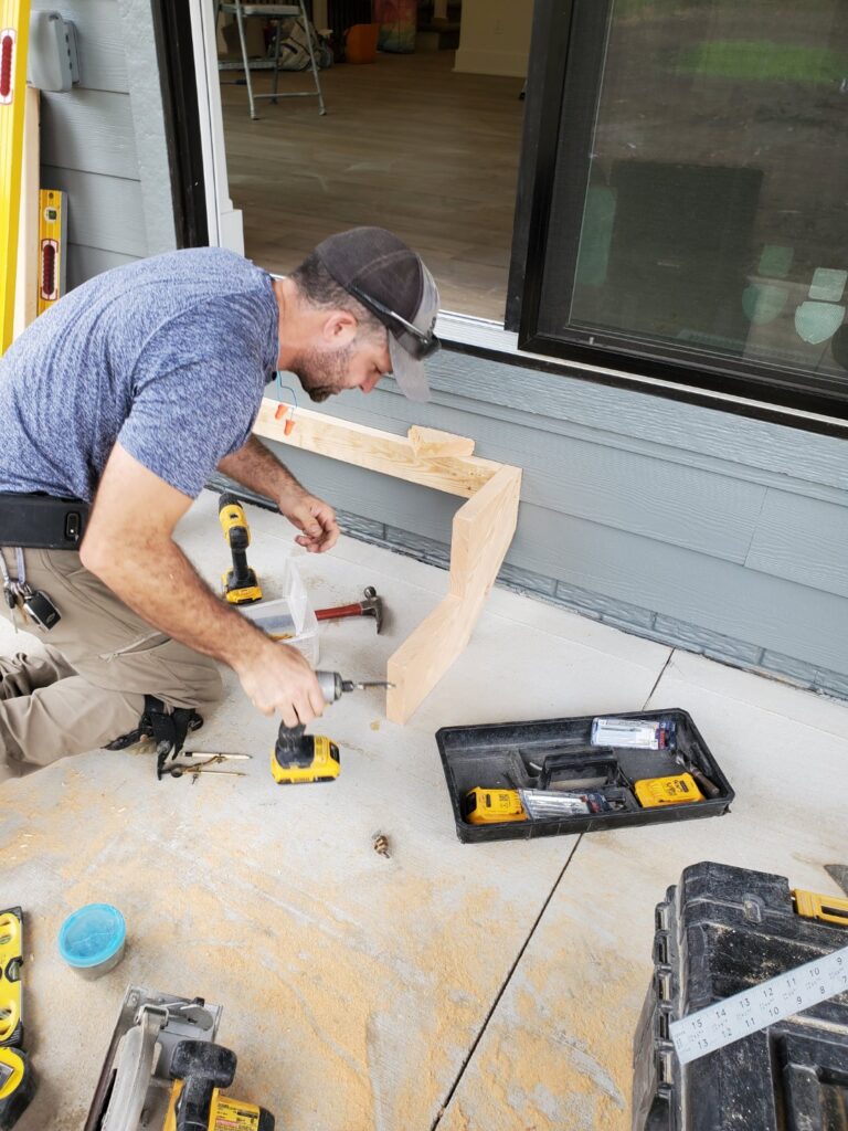 Carpenter installing a wooden trim piece on a construction site.