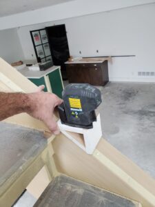 Laser level being used to check alignment during trim installation in an unfinished room.