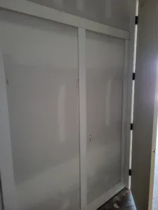 Primed white bifold door panel installed with visible hinges, unfinished opening, no casing yet