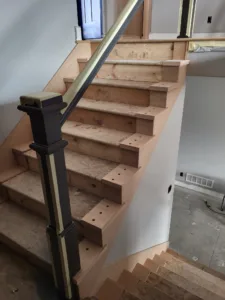 Unfinished wood stair treads with drilled baluster holes, newel post, and diagonal rail brace