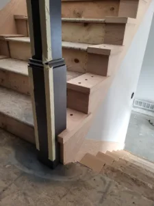 Black metal round newel post installed at stair base with unfinished wood treads and risers