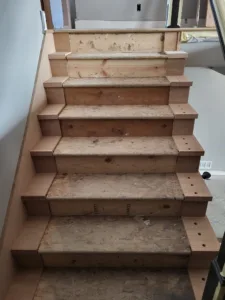 Raw wood stair stringer with stepped end cap blocks and a row of drilled holes, unfinished