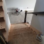 Black metal wall-mount handrail installed on staircase with finished wood treads and white painted walls.