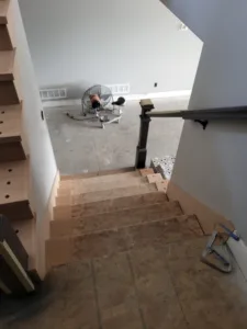 Black metal handrail mounted to the wall above a staircase with wood-toned treads, seen from a tiled landing.