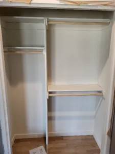 Closet with a hanging rod, center divider, and open shelving, raw wood shelf edges, painted white interior.