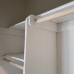 Closet face-frame with two painted white vertical supports and natural wood hanging rods installed at upper and lower levels.