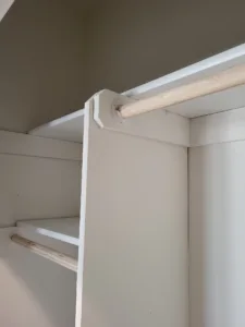 Closet corner with a natural wood hanging rod mounted on a painted white face-frame support.
