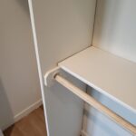 Closet hanging rod with natural wood finish installed on painted white wall with casing trim.