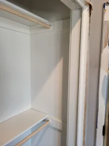 Closet interior with upper and lower hanging rods installed, painted walls, trimmed door opening.