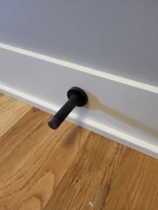 Black door bump mounted on painted white baseboard above hardwood flooring