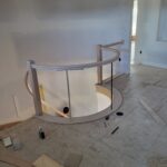 Curved handrail with horizontal metal rods and wood cap installed on curved wall structure during construction.
