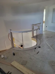 Curved handrail with a wood cap installed around a stairwell opening, guard infill below, unfinished walls.