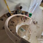 Curved staircase with notched skirt boards being installed during active framing and trim work.