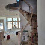 Spiral staircase with curved handrail and wood balusters mid-construction; job site overview with tools and materials visible.
