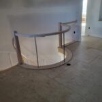 Curved staircase railing with wood handrail and horizontal metal rod balusters, trim stage.