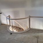 Curved stair railing with wood newel posts and metal balusters installed, raw wood finish ready for paint.