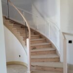 Curved staircase with wood treads, risers, and curved handrail installed; walls and newel posts primed but not yet painted.