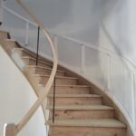Curved stair with horizontal black metal cable railing and wood handrail, raw wood treads and risers ready for finish.