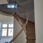 Curved stair with horizontal metal rod railing installed between newel posts; wood handrail and treads unfinished.