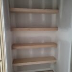 Four floating wood shelves installed in closet alcove, raw wood not yet painted or stained.