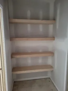Four floating raw wood shelves stacked in a narrow closet alcove, unfinished and unpainted.