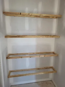 Unfinished wood shelf frames fastened to a wall in stacked rows, ready for finish wrap.
