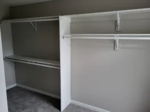White painted closet shelf and rod system installed in a corner closet with gray carpet floor