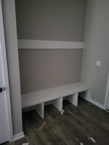 Built-in bench nook with open cubby dividers below a single shelf, painted gray, wood floor.
