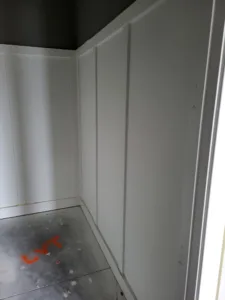 Painted white flat panel wall paneling in a room corner with construction dust on the floor