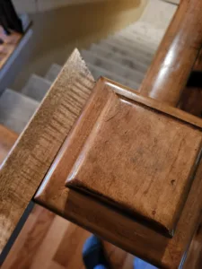 Stained wood newel post with a rounded profile and polished cap, finished detail shot.