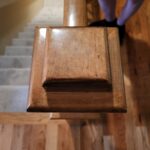 Finished wood newel post cap with beveled profile and stain detail at stair landing.