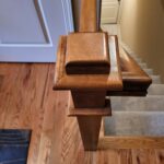 Finished wood newel post with stacked base blocks at stair bottom, stained cherry or similar hardwood.