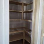 Corner closet shelving with multiple tiers and wooden cleats, raw wood ready for finish.