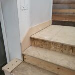 Stair landing in progress with raw wood treads, unfinished walls, and handrail framing visible.