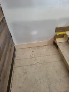 Unfinished baseboard trim installed at an inside corner over OSB subfloor, ready for paint.