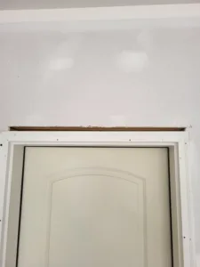 Arched panel door hung in unfinished jamb, exposed header framing above with casing not yet installed