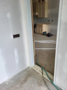 Primed door jamb corner at drywall stage, no casing or slab yet, opening into a kitchen under construction