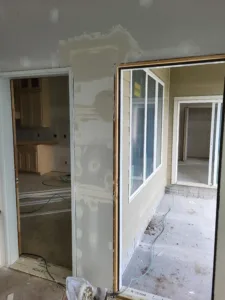 Drywall stage doorway opening into a kitchen, with a window jamb and taped seams visible nearby.