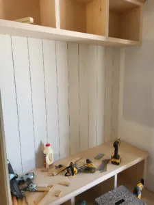 Unfinished vertical shiplap paneling above a built-in bench, primed but not yet painted