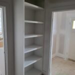 Custom built-in bookcase with six shelves, white painted finish, installed in corner between two interior doors.