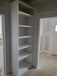 Tall built-in bookcase with several shelves positioned in a hallway corner near a doorway.