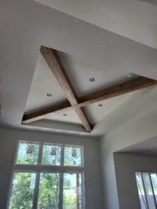 Unfinished wood ceiling beams crossing in an X pattern above a vaulted window wall