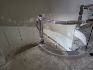 Curved handrail and newel post wrapped for protection, wainscot paneling visible below, during installation.