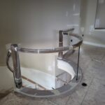 Curved handrail sections and fittings installed on curved stair opening with newel posts and brackets, wrapped for protection during construction.