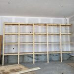 Multi-tier closet shelving system with raw wood frame and particle board shelves, ready for paint.